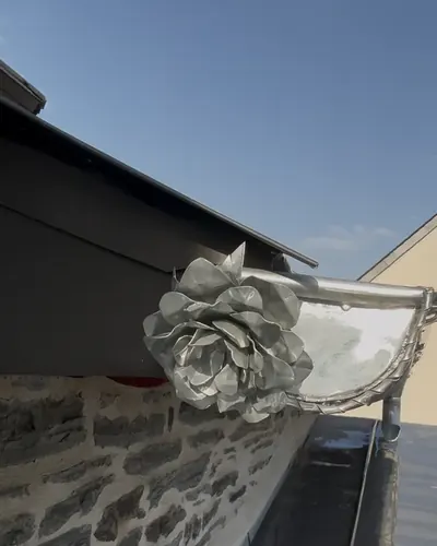 Rose en zinc aux pétales façonnés à la main, soudée sur la naissance d'une gouttière